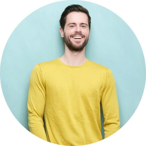 Man with a beard in a yellow sweater smiles against a light blue background.