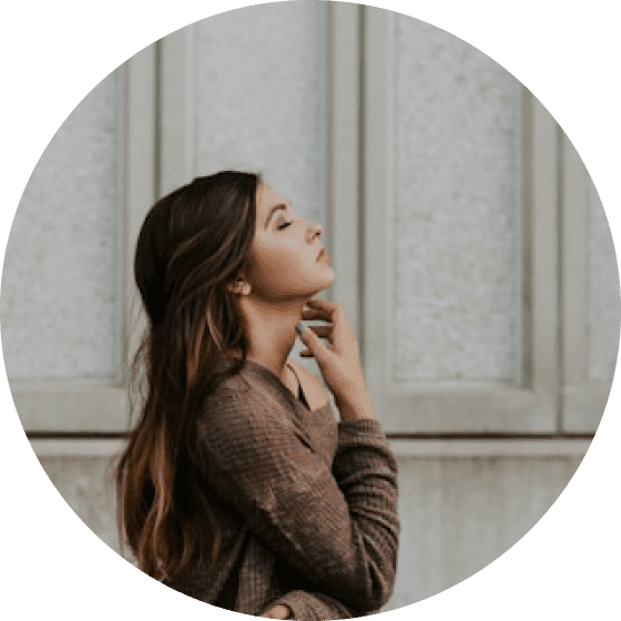 Woman with long hair in profile, wearing a brown shirt, stands in front of a textured wall.